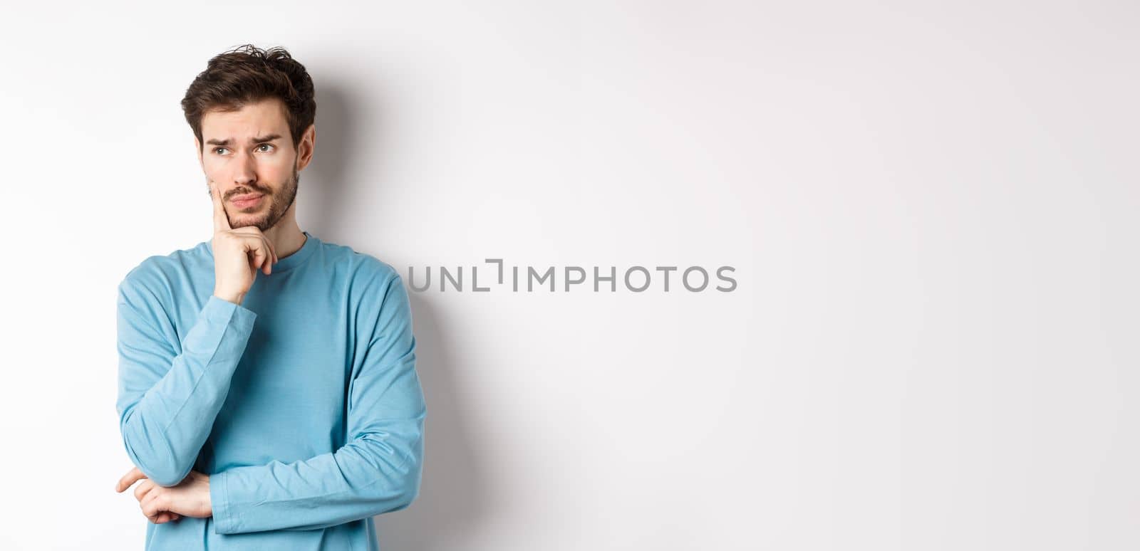 Young bearded man looking pensive and frowning, thinking about problem or trouble, standing worried against white background.