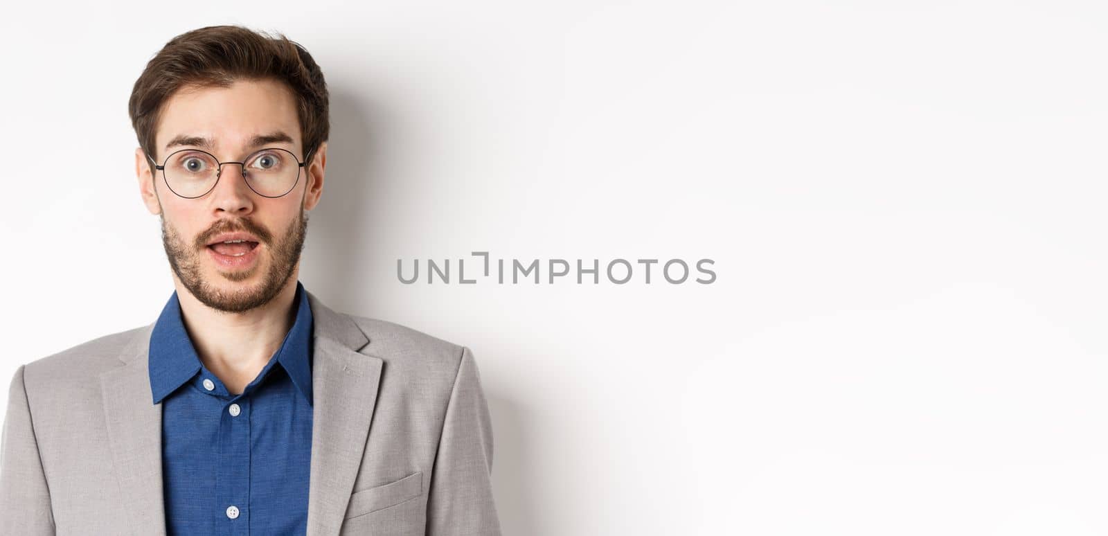 Close-up of surprised business man in glasses and suit gasping amazed, hear good news, standing on white background by Benzoix