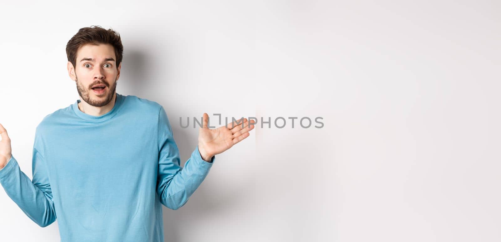 Unbelievable. Amazed young man looking with disbelief, spread hands sideways and staring impressed, standing over white background by Benzoix