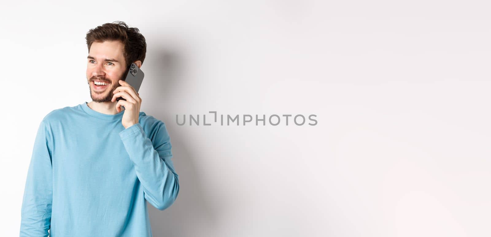 Technology concept. Joyful man enjoying phone call, talking on smartphone and smiling, standing in casual shirt over white background.