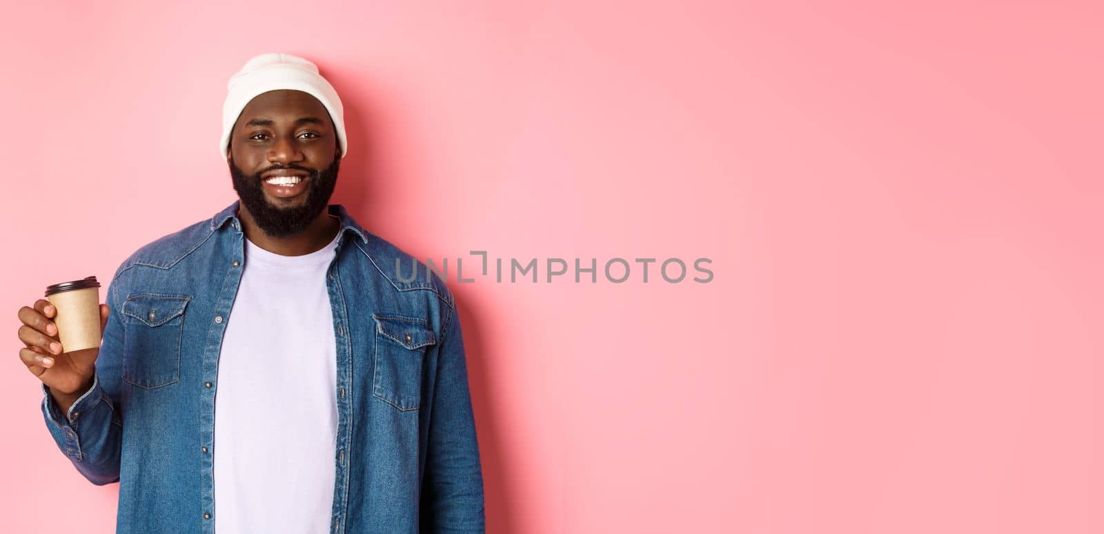 Handsome modern Black man drinking takeaway coffee, smiling and looking satisfied at camera, standing over pink background by Benzoix