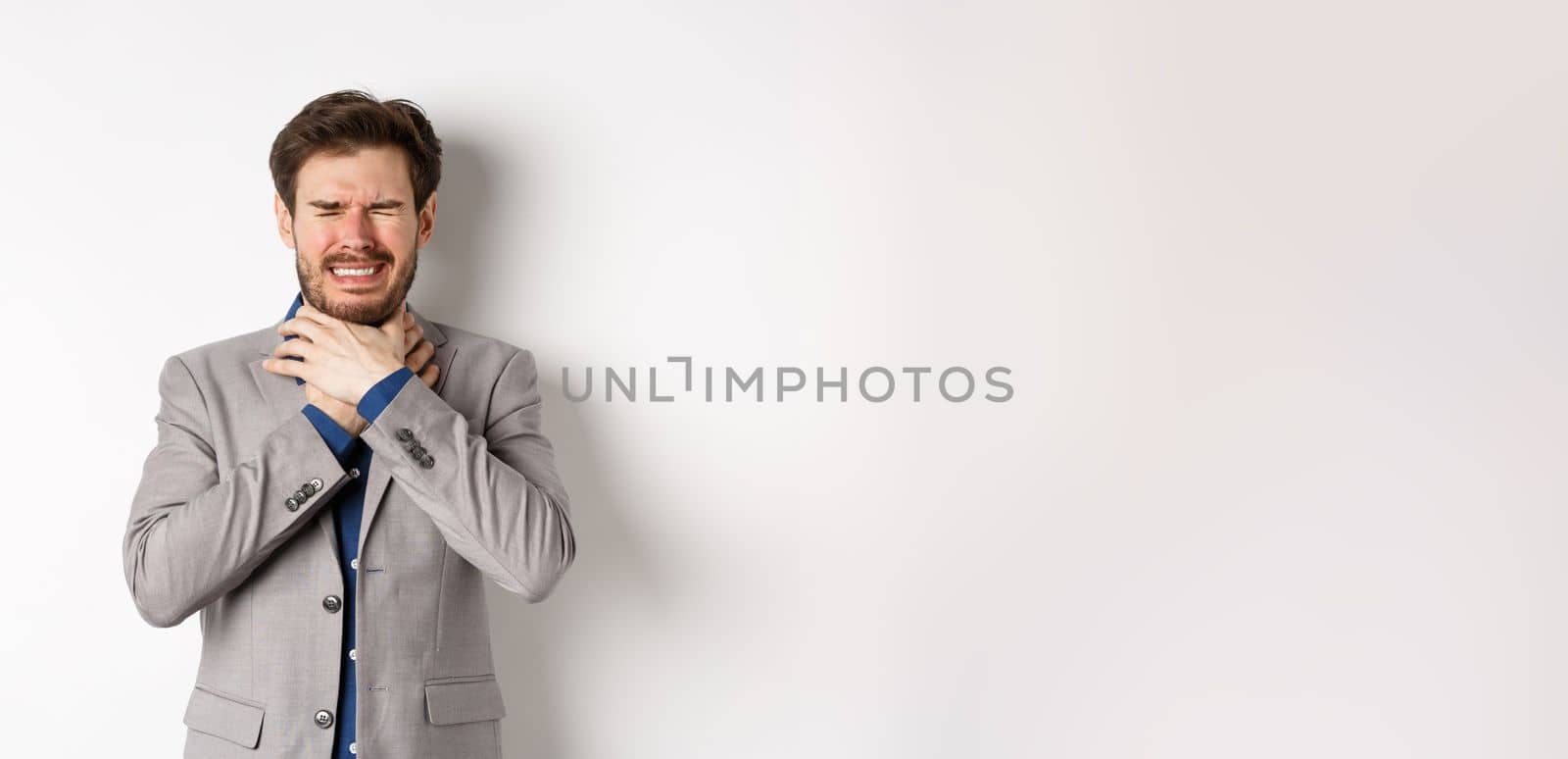 Crying man in suit holding hands on neck and look distressed, feel sick with sore throat, standing on white background by Benzoix