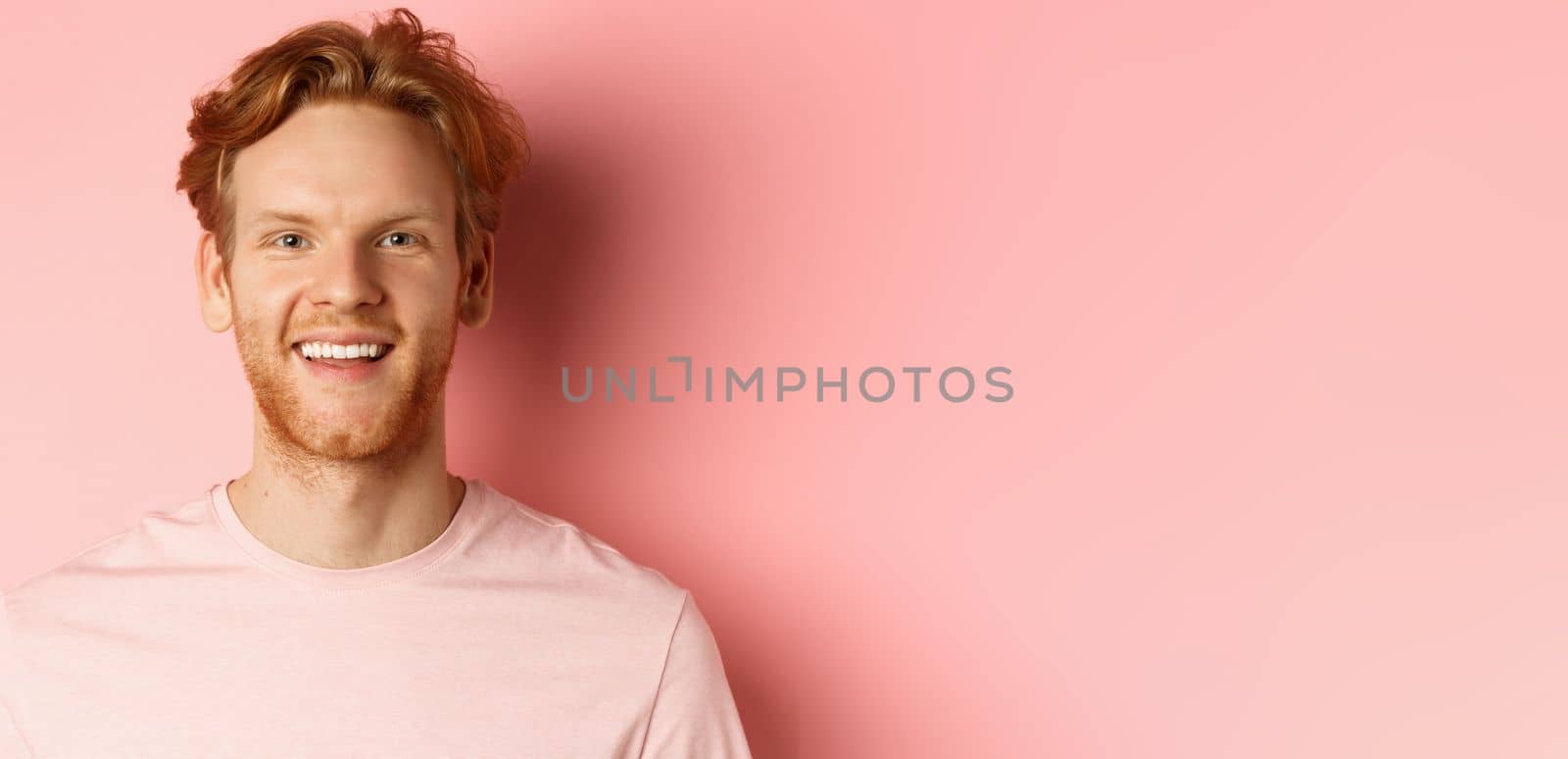 Headshot of happy redhead man with beard and white teeth, smiling excited at camera, standing over pink background by Benzoix