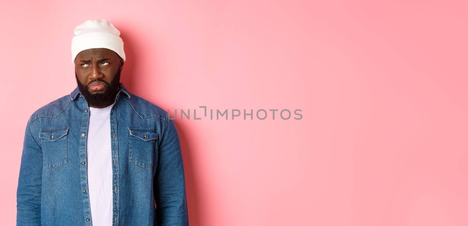 Disappointed and sad Black man, sulking and whining, looking at upper left corner with offended and jealous grimace, standing over pink background by Benzoix