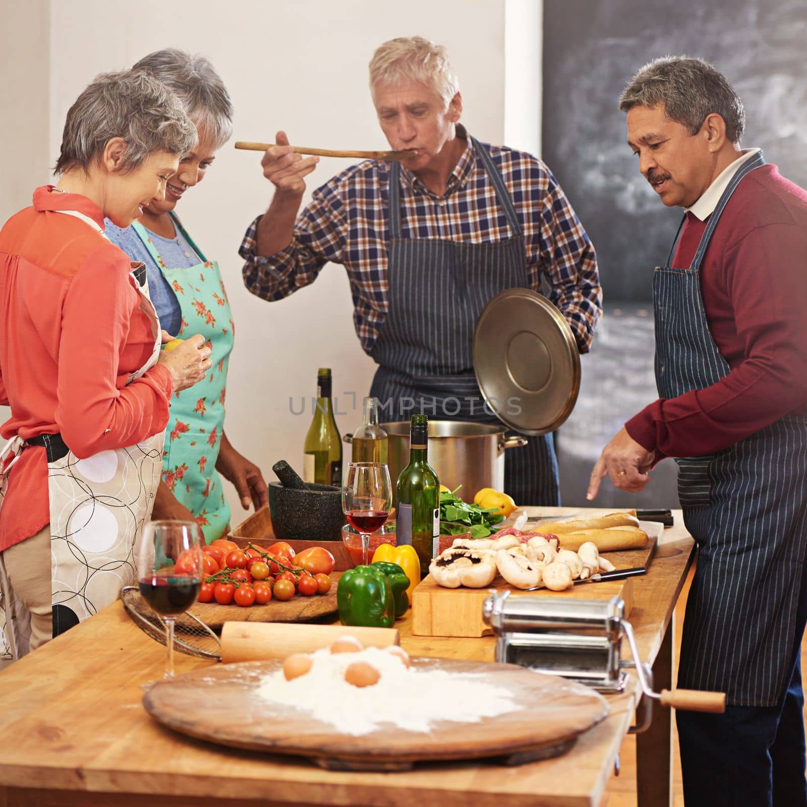 The secret is one heaping spoon of love. a group of seniors cooking in the kitchen. by YuriArcurs