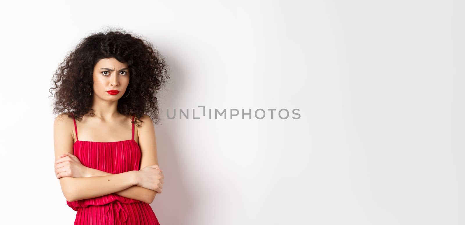 Sad and offended caucasian woman in red dress frowning, cross arms on chest and sulking, feeling mad at you, standing over white background by Benzoix