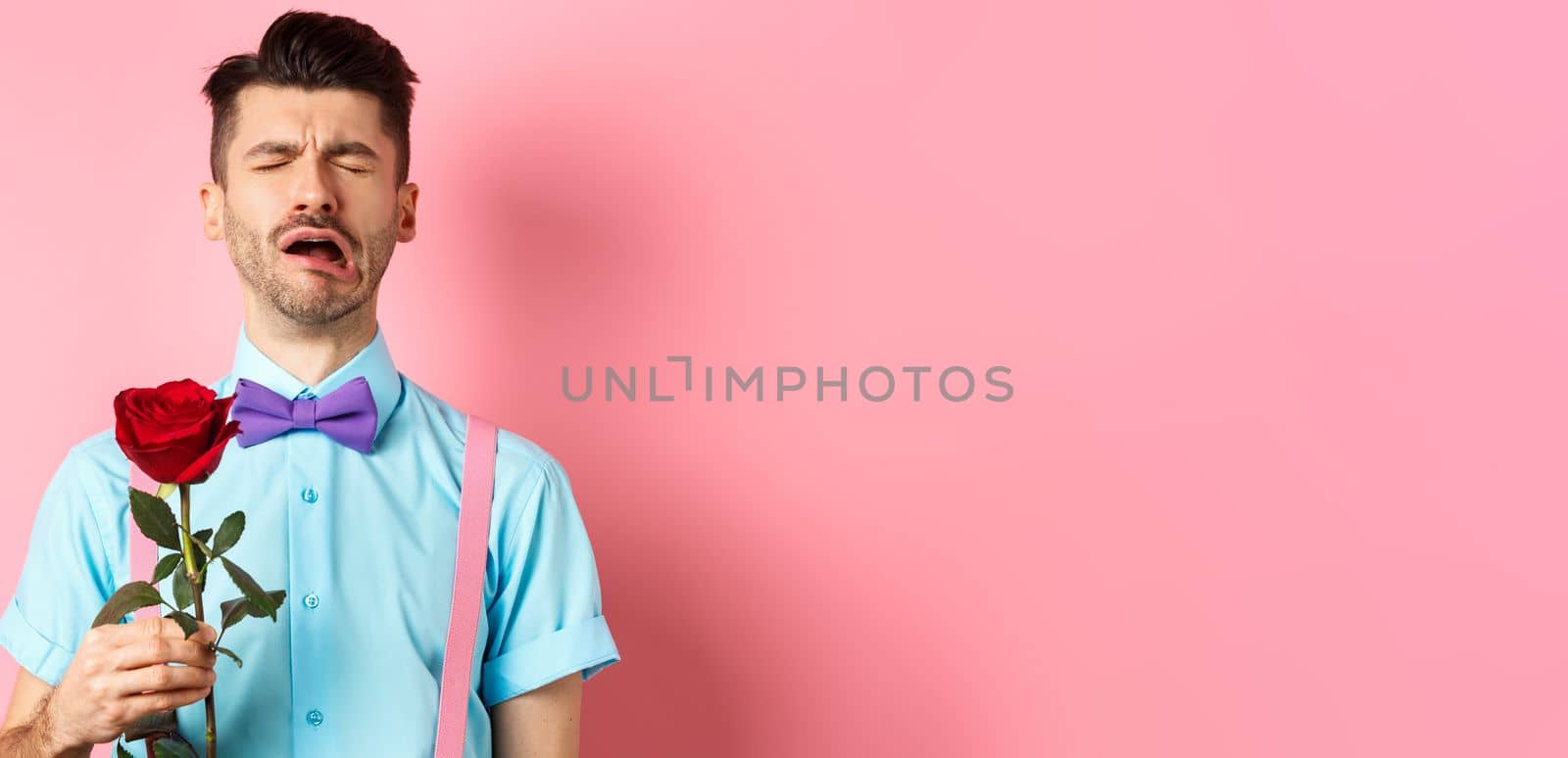 Heartbroken guy in funny bow-tie crying over girlfriend, standing alone with red rose on pink background and sobbing, break-up on Valentines day by Benzoix