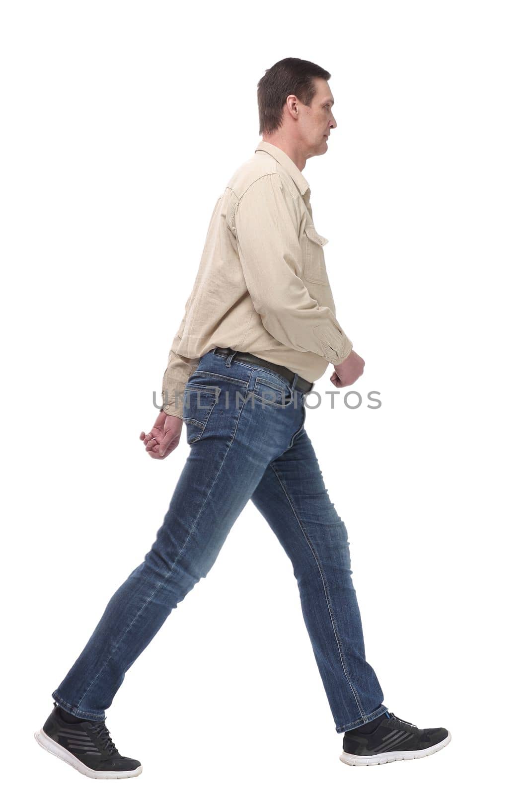 full length side view picture of a casual young man walking looking at camera, isolated on white