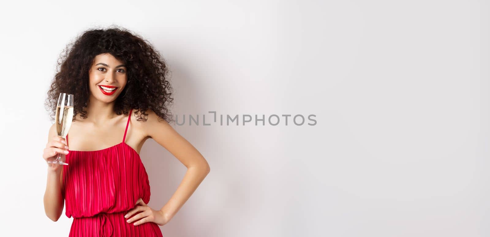 Sassy young woman in elegant red dress, posing with glass of champagne on white background, having romantic date on valentines day by Benzoix