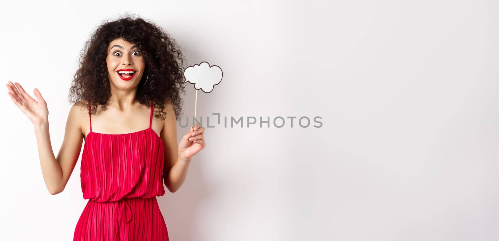 Happy young woman in red dress, holding comment cloud and looking surprised, standing over white background. Copy space