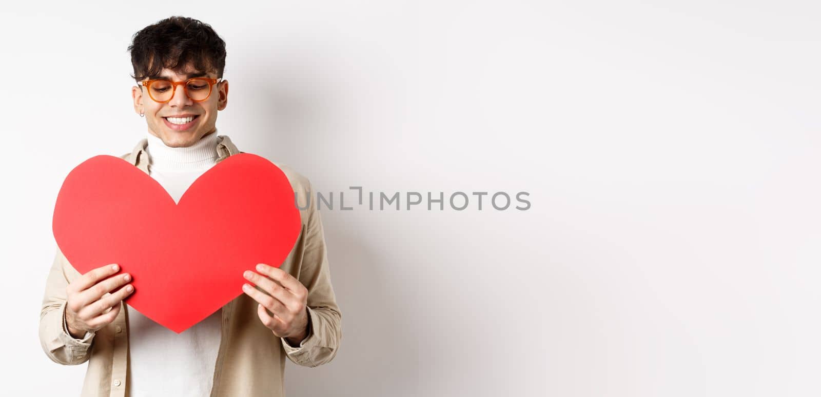 Handsome and stylish man in sunglasses, prepare surprise postcard for girlfriend on Valentines day, holding big red heart cutout and smiling happy, standing over white background.