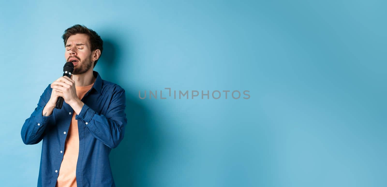 Romantic guy singing in microphone, performing on stage, standing on blue background by Benzoix