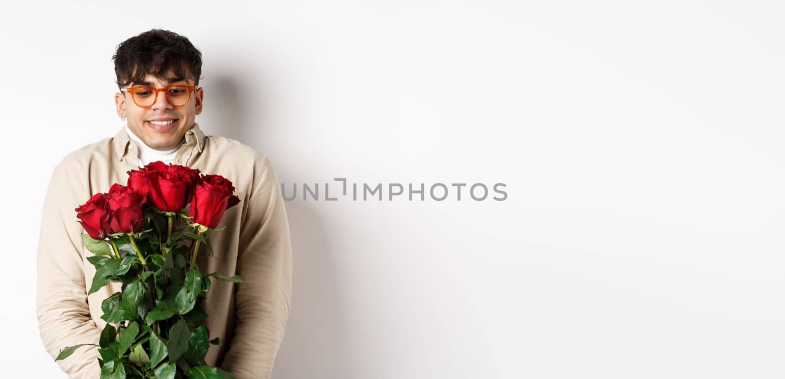 Cheerful gay man receive red roses from boyfriend, looking excited and smiling, having romantic date on Valentines day with lover, standing over white background.