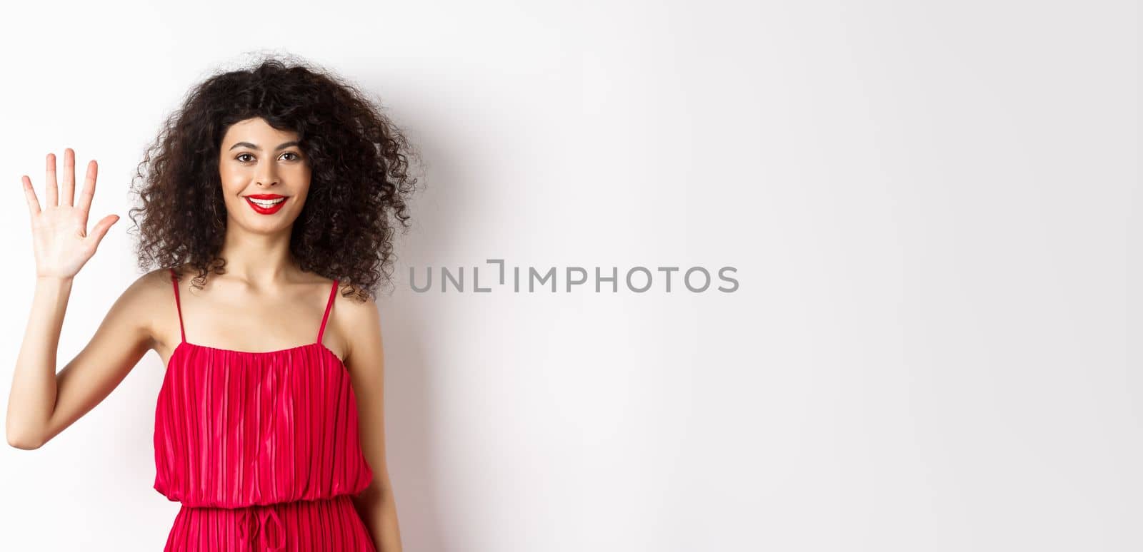 Cheerful young woman with makeup and red dress, showing five fingers and smiling, standing over white background by Benzoix