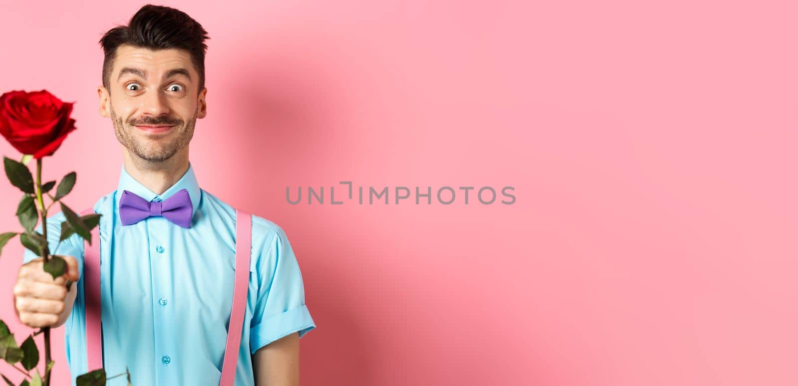 Valentines day and romance concept. Funny guy with moustache giving red rose and smiling, making romantic gesture on date, standing over pink background.