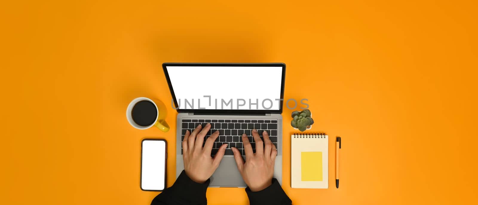 From above view of man hands typing laptop computer over yellow background. Blank screen and copy space for text.