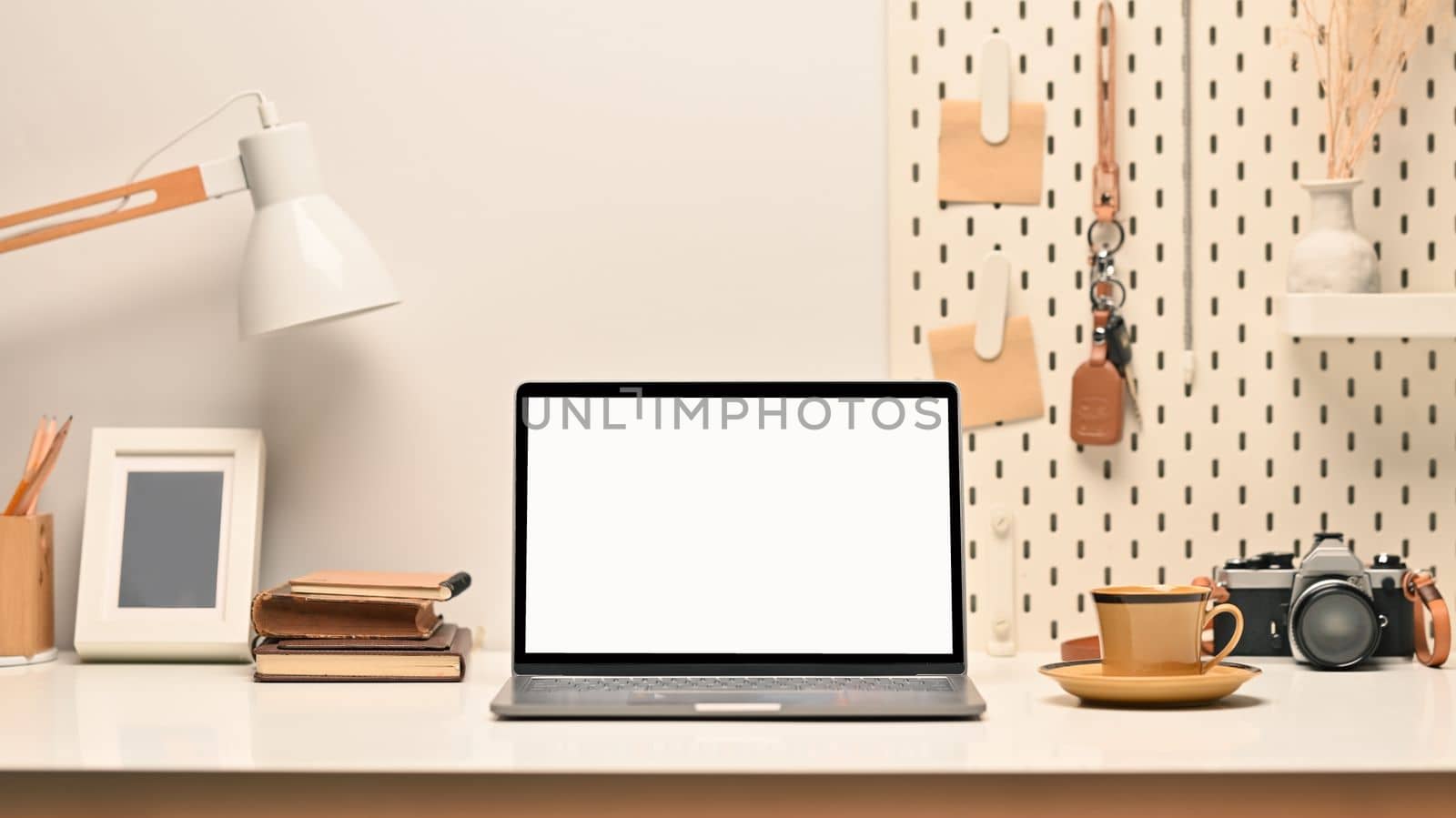 Comfortable workplace, laptop with blank screen, picture frame , camera and lamp on white table by prathanchorruangsak