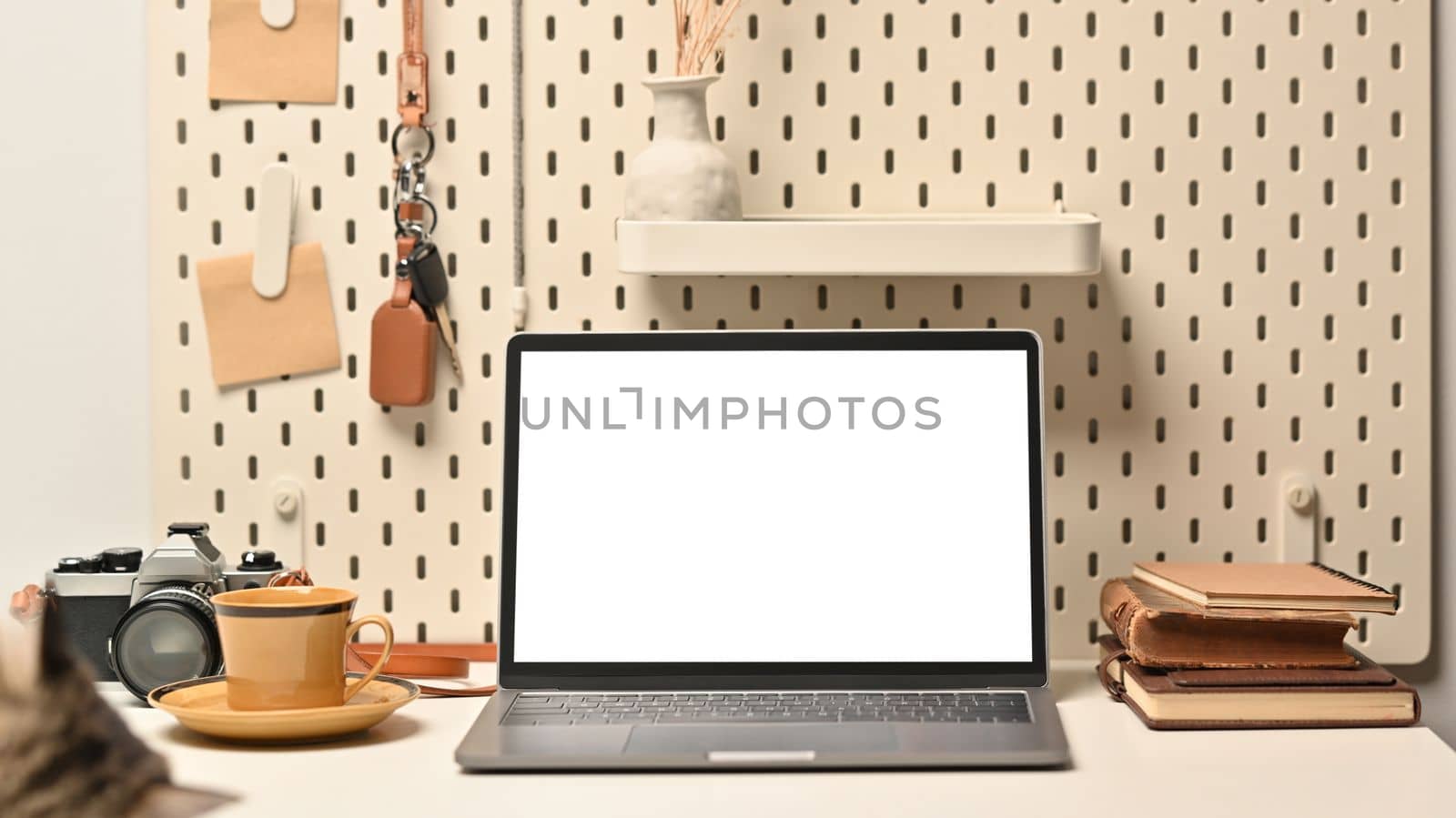 Front view of white blank screen laptop, camera, books and coffee cup on white table by prathanchorruangsak