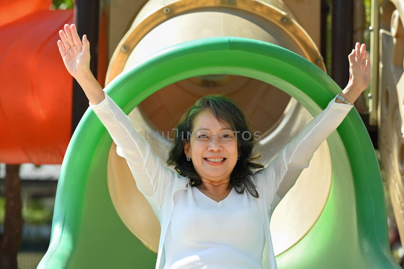 Overjoyed mature grandma having fun on colorful slide. Happy moment, family and love concept.