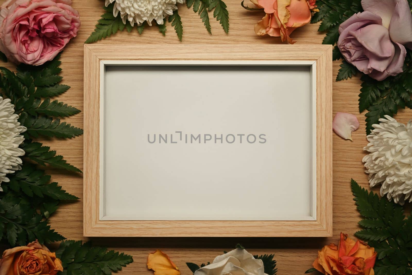 Wooden photo frame surrounded by fresh flowers and green leaves. Floral frame, spring or summer background.