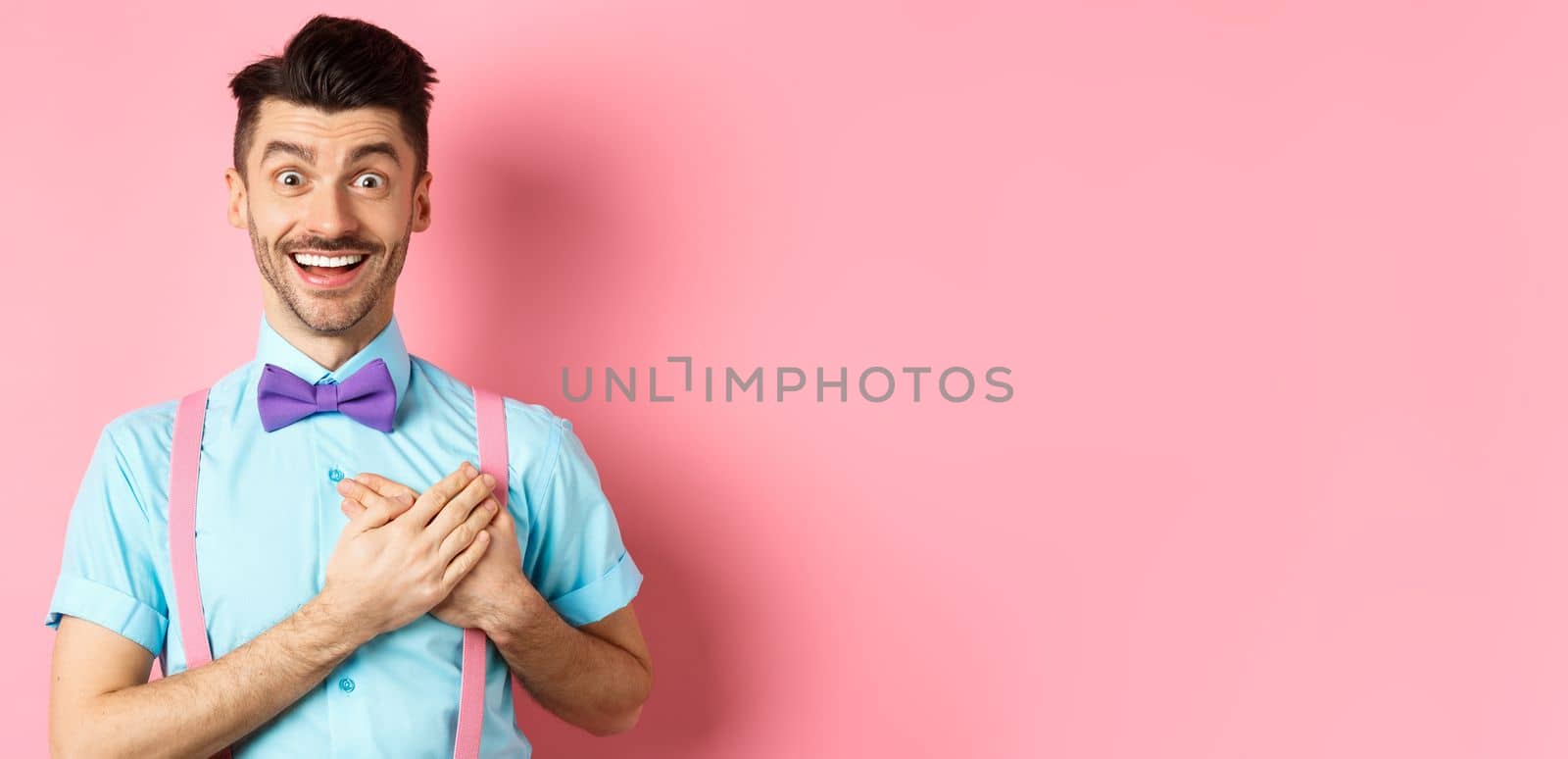 Valentines day and romance concept. Happy man in love holding hands on heart and looking with sympathy at lover, standing on romantic pink background.