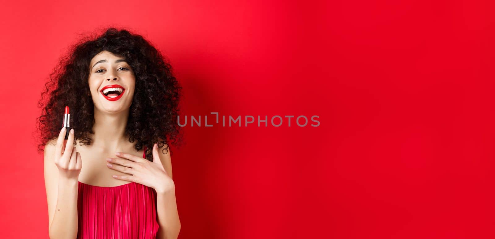 Elegant woman in dress, showing red lipstick and laughing, standing over studio background. Copy space