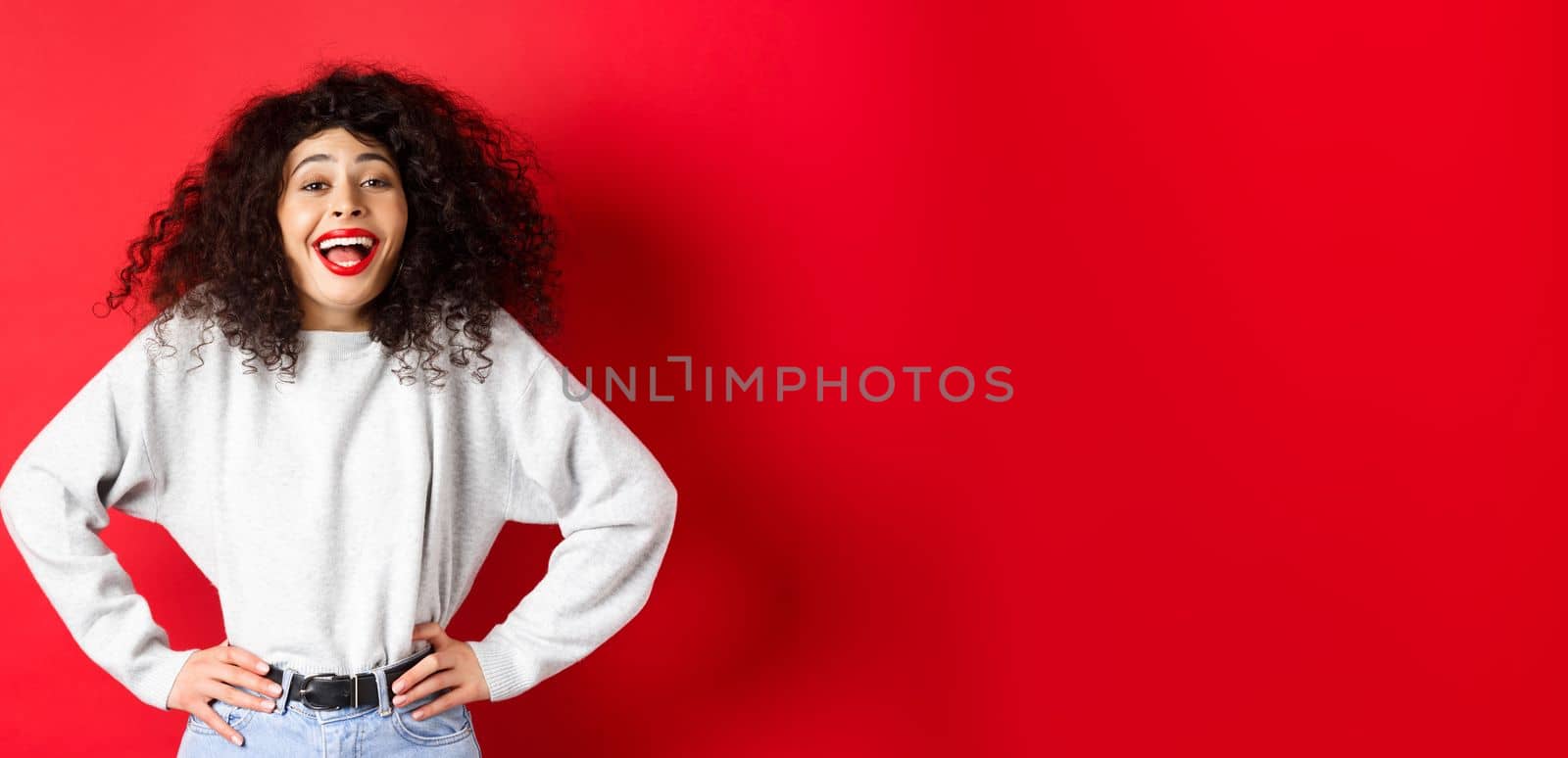 Excited positive woman laughing and smiling, feeling upbeat, looking at funny promo, standing on red background.