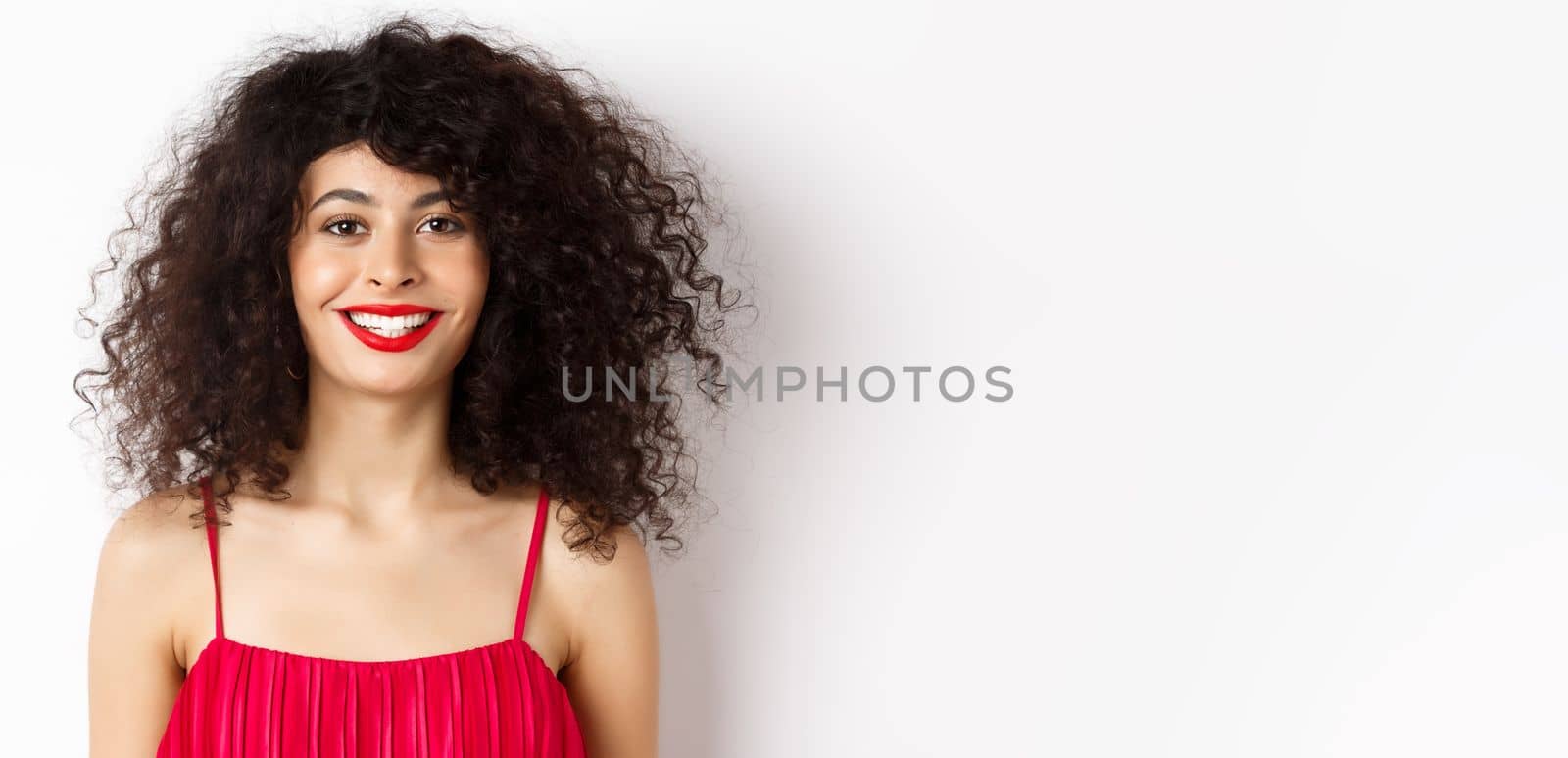 Close-up of beautiful woman with curly hairstyle, wearing red dress and lipstick, smiling happy at camera, white background by Benzoix