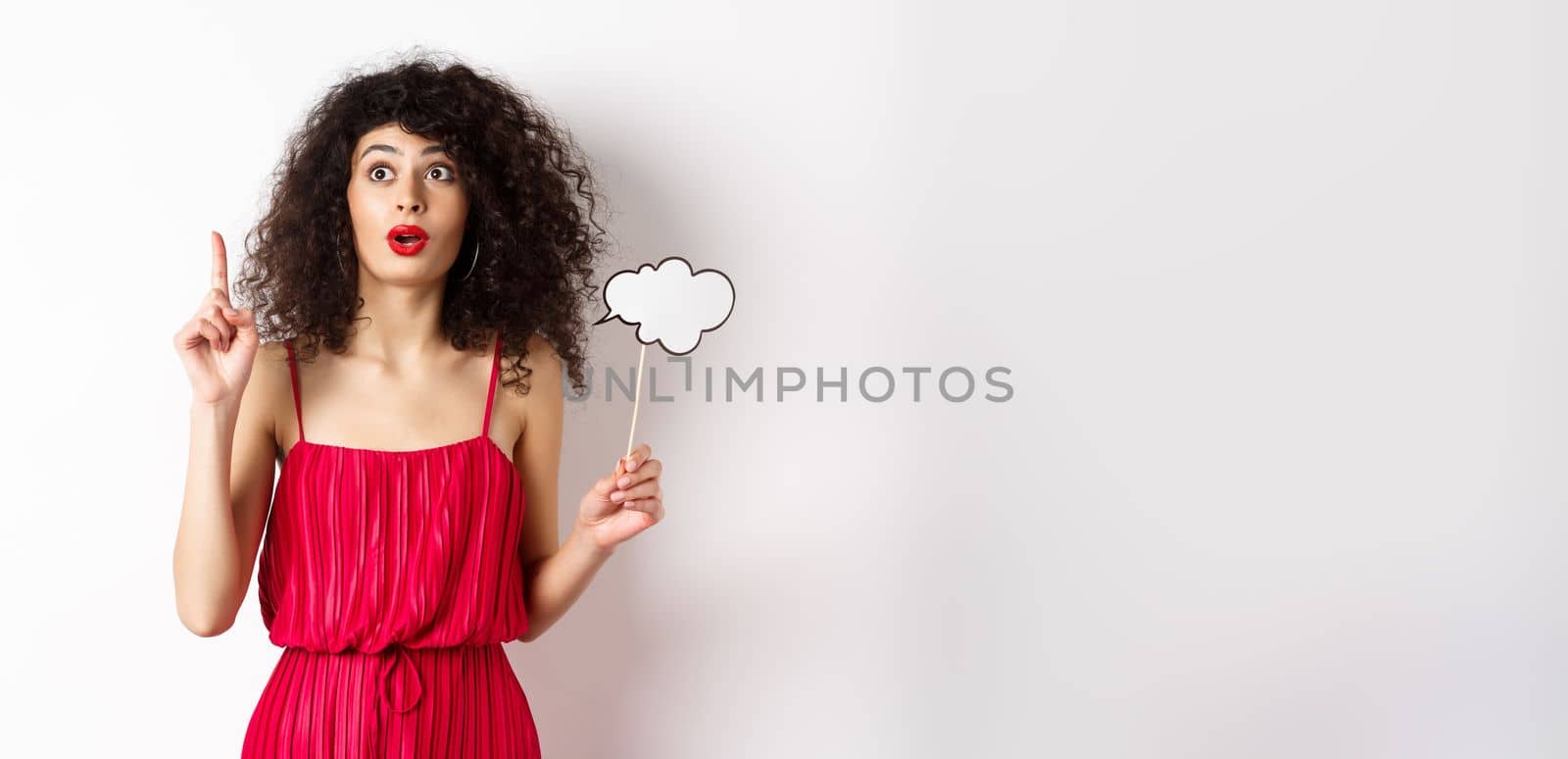 Excited fashionable woman in red dress pitching an idea, raising finger in eureka sign, holding thought cloud, standing on white background.