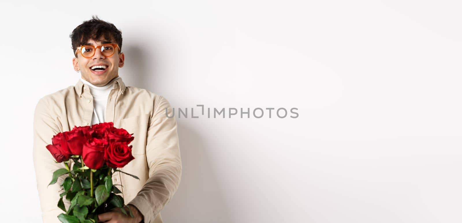 Man in love holding red roses and looking tenderly at camera, staring at lover with happy face, celebrating Valentines day with girlfriend, standing over white background by Benzoix