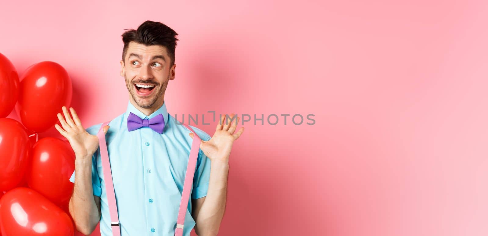 Love and romance concept. Happy man screaming from fantastic news, shouting wow and smiling amused, checking out special offer on Valentines, standing near red hearts balloons.