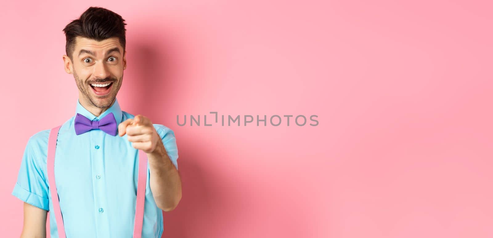 Cheerful smiling man in bow-tie pointing finger at camera, inviting or picking you, searching for candidate, standing over pink background by Benzoix