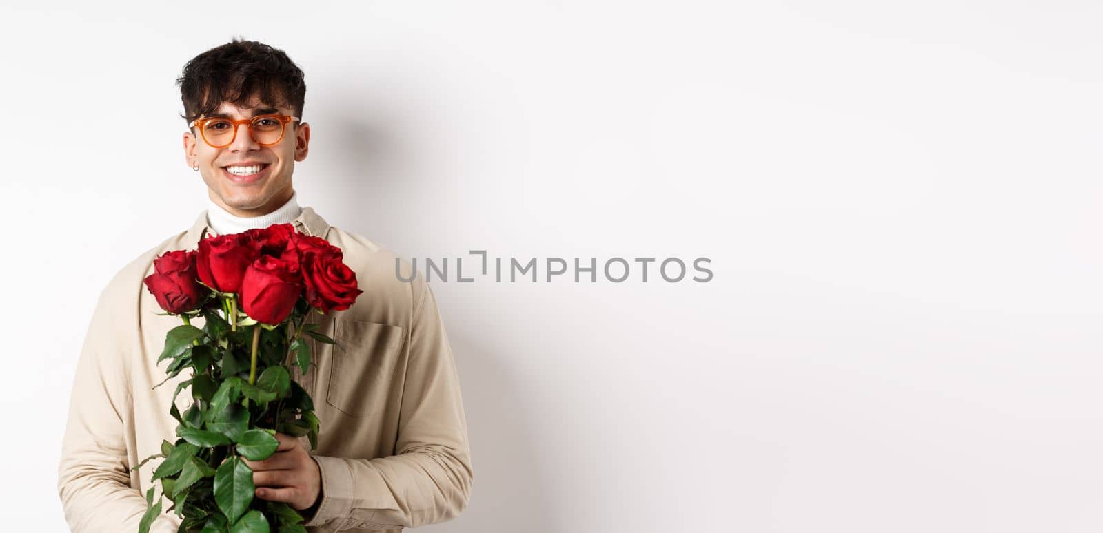 Handsome hipster guy waiting for his lover with bouquet of roses. Young man with flowers standing on Valentines day over white background.