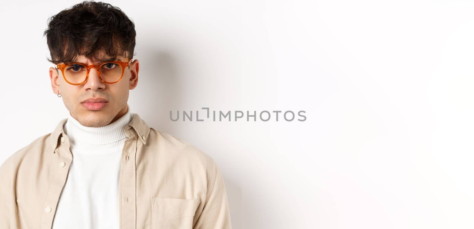 Close up portrait of angry frowning guy looking with dispise, standing mad on white background, wearing glasses.