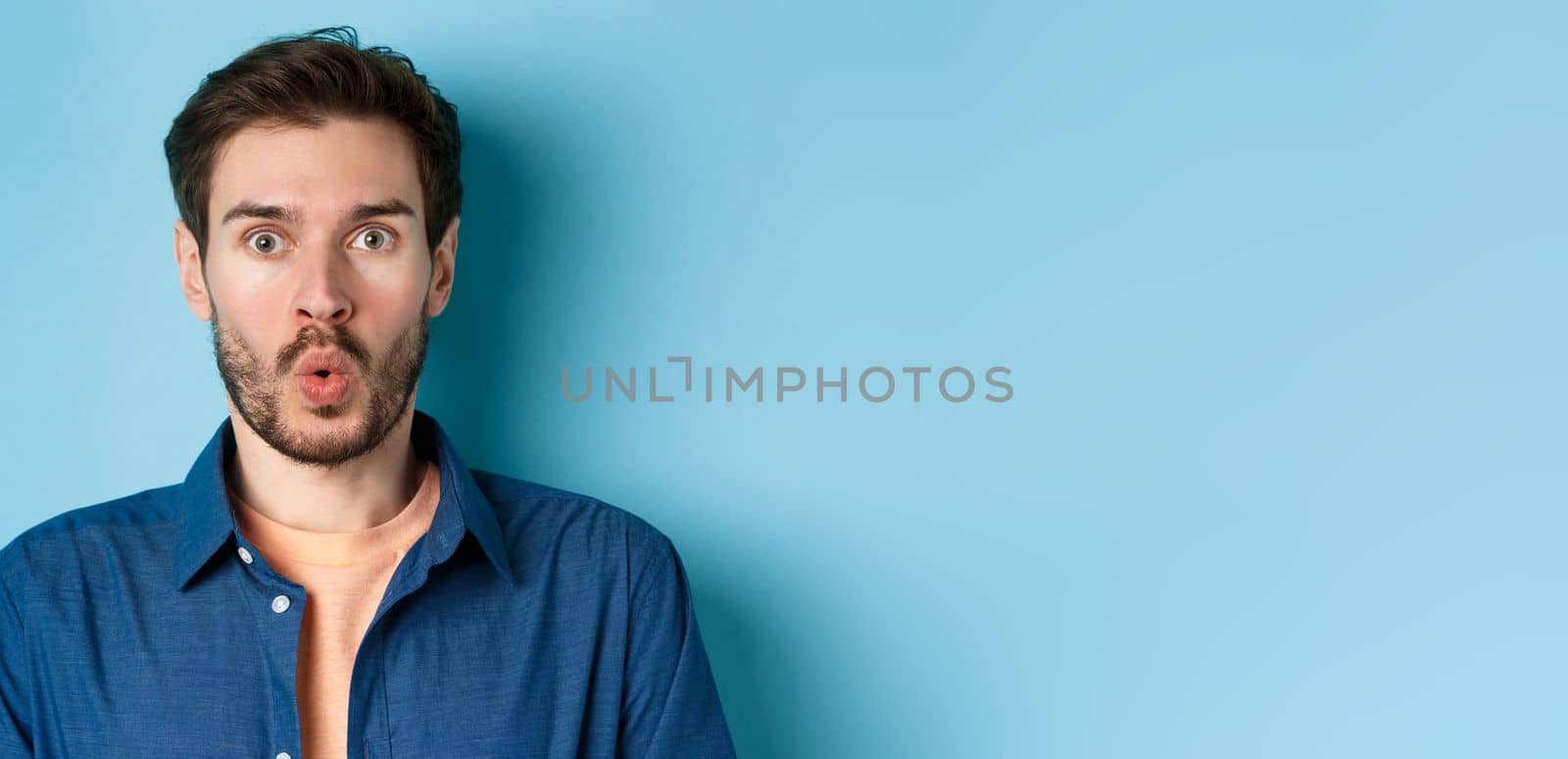 Close up portrait of amazed and surprised man saying wow, staring impressed at camera, checking out cool offer, standing on blue background by Benzoix