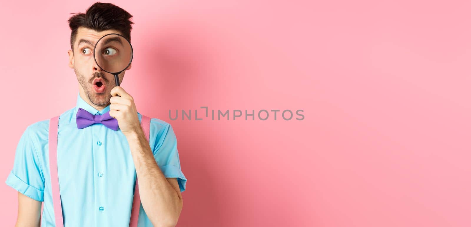 Surprised man saying wow and look aside through magnifying glass, checking out promo offer, standing over pink background by Benzoix