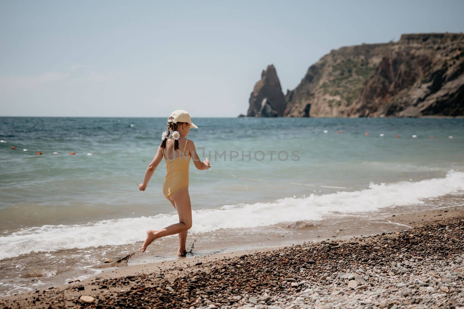 Cute little girl running along the seashore against a clear blue sea and rejoices in the rays of the summer sun. Beautiful girl in yellow swimsuit running and having fun on tropical beach. by panophotograph