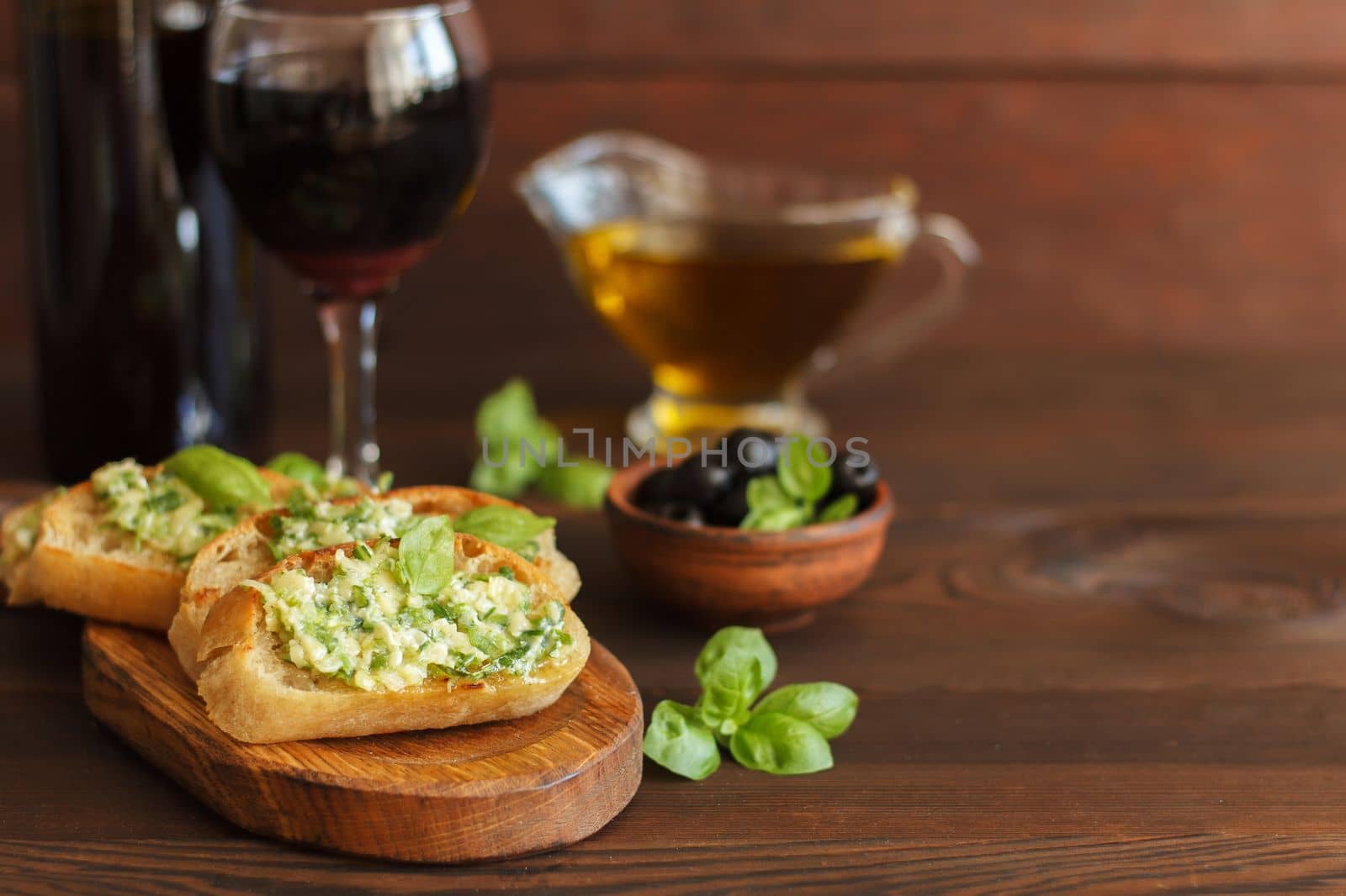 Delicious bread with garlic, cheese and herbs, red wine and olives on a wooden table.Copy space