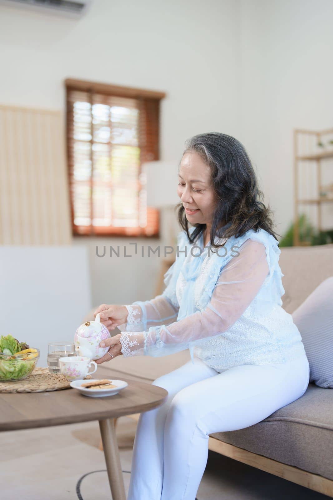 Portrait of an elderly Asian woman drinking healthy tea while eating vegetable salad and snack. by Manastrong