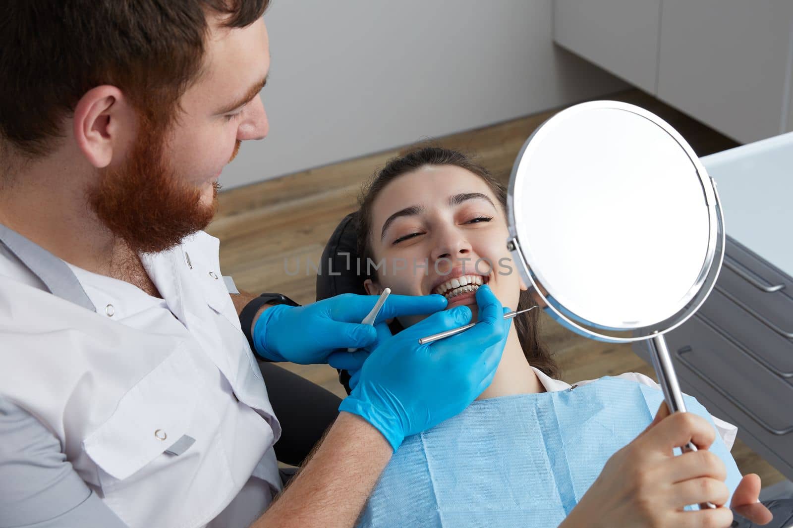 Young Woman Looking At Mirror With Smile In Dentist Office