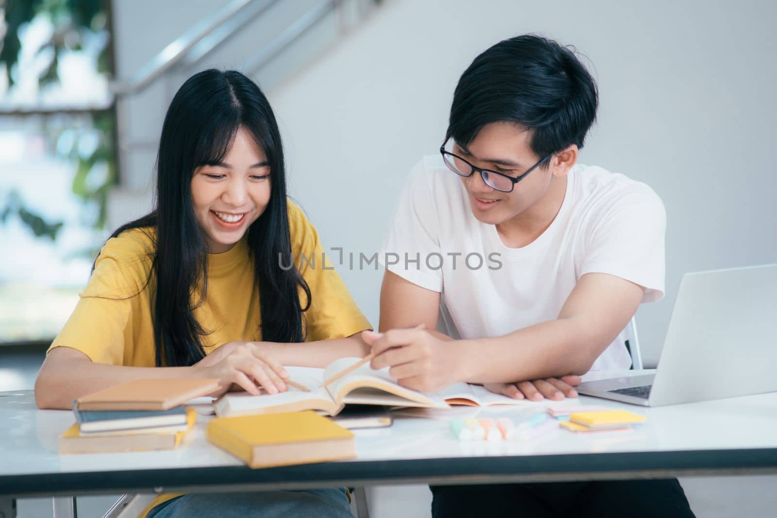 Young asian university students are studying for an exam. There are tutor books with friends. They are classmates that try to help each other. They have been tutoring for many hours in the campus.