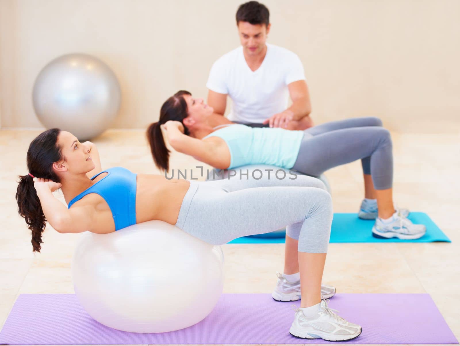 Safe sit-ups for weak backs. Young woman doing a sit up during a pilates class with the help of an instructor. by YuriArcurs