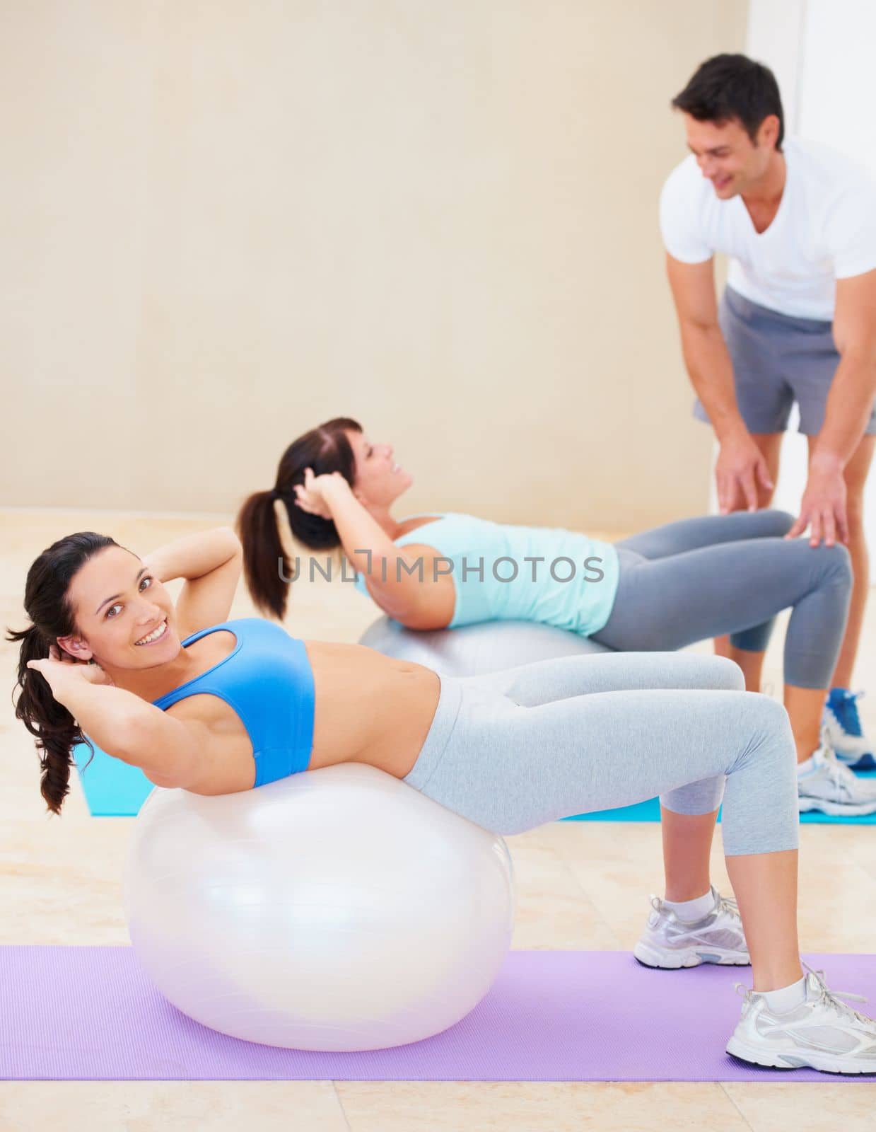 She knows her workouts will pay off. Young woman doing a sit up during a pilates class with the help of an instructor. by YuriArcurs