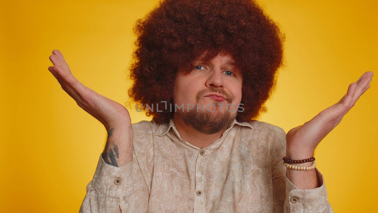 I dont know what to say. Confused man with afro hairstyle feeling embarrassed about ambiguous question, having doubts, no idea, no answer, being clueless and uncertain. Young guy on yellow background