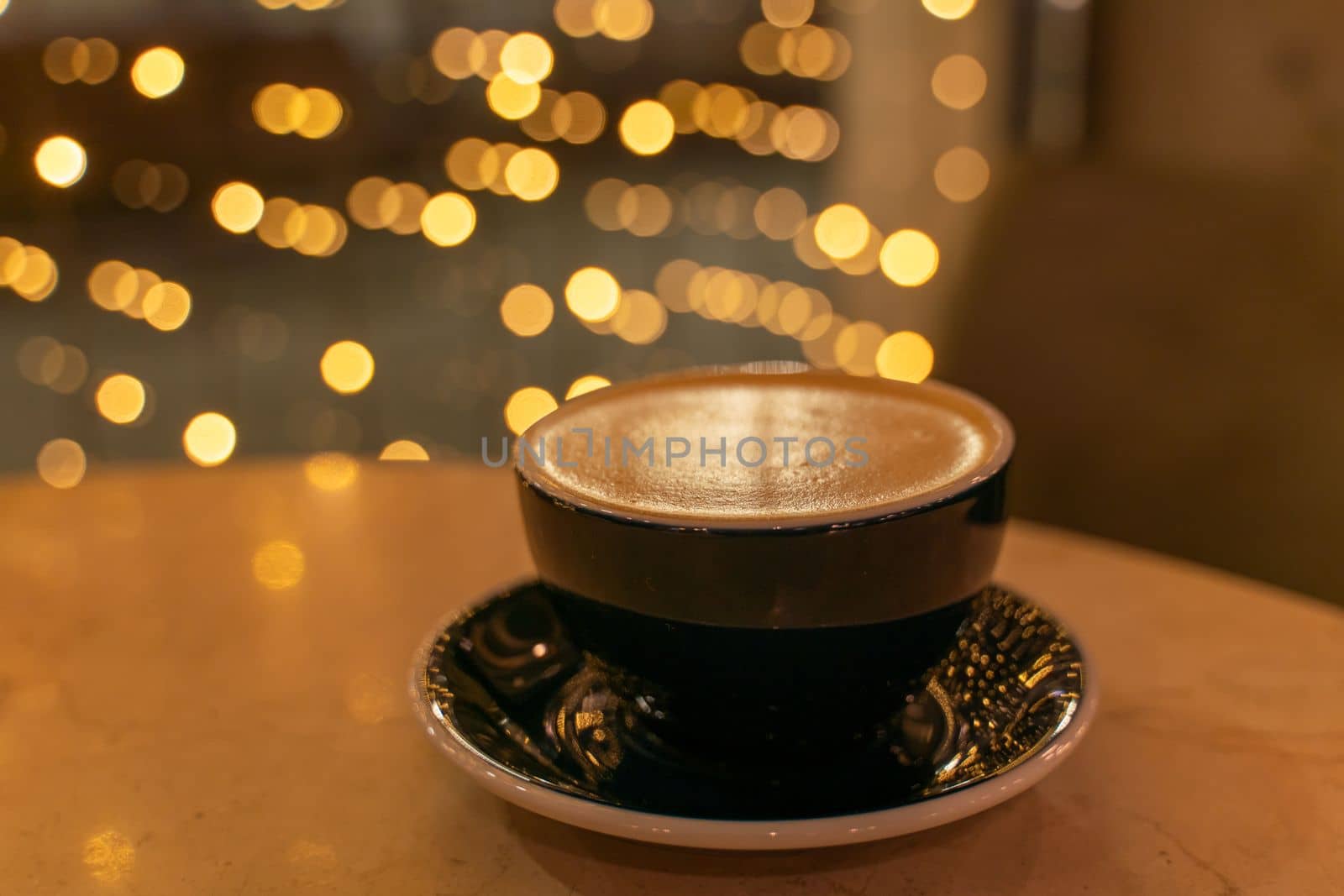 A cup of latte coffee with heart-shaped foam on a table in a cafe, in the background, the lights in a blur are reflected on the table