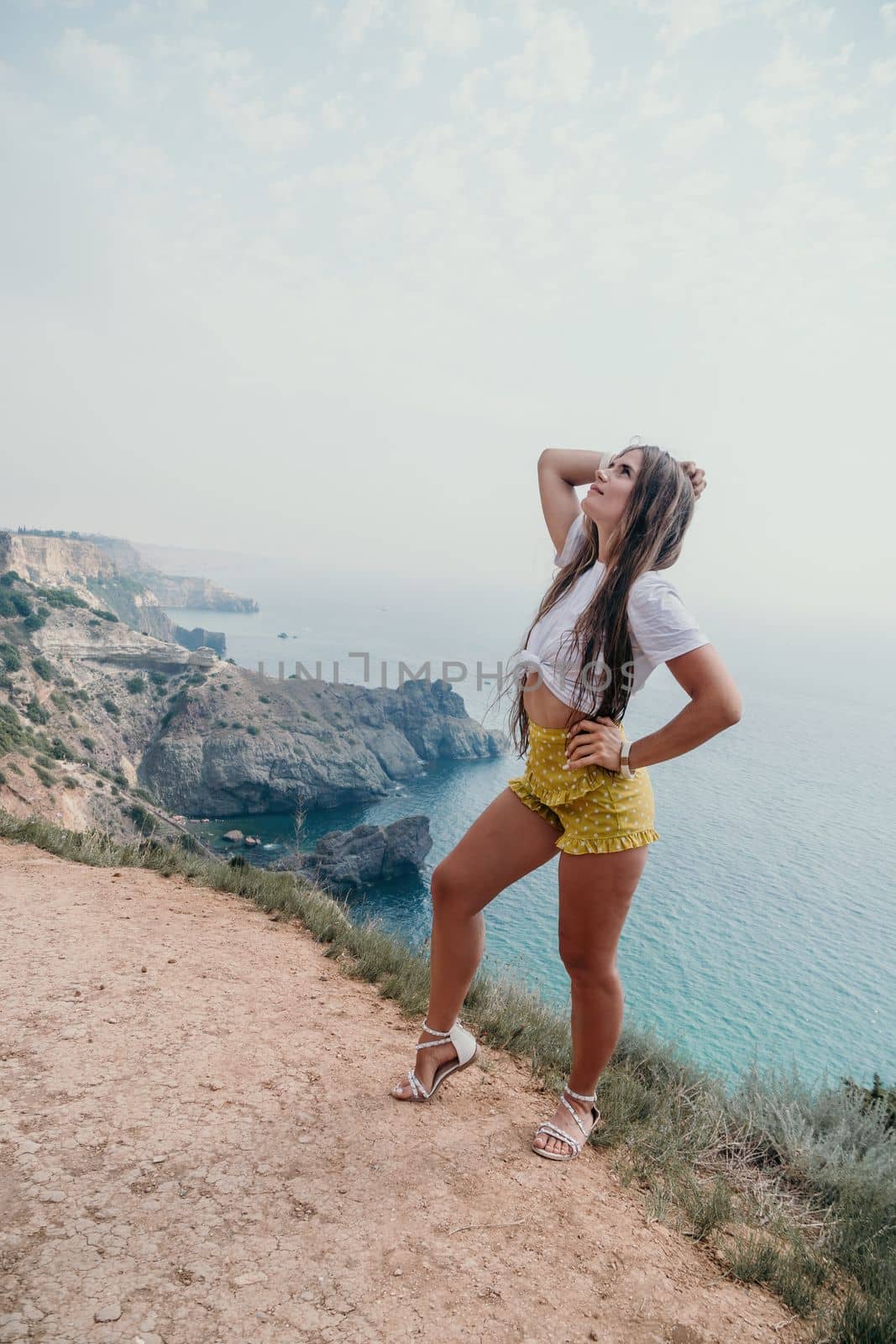 Woman travel sea. Happy tourist taking picture outdoors for memories. Woman traveler looks at the edge of the cliff on the sea bay of mountains, sharing travel adventure journey.