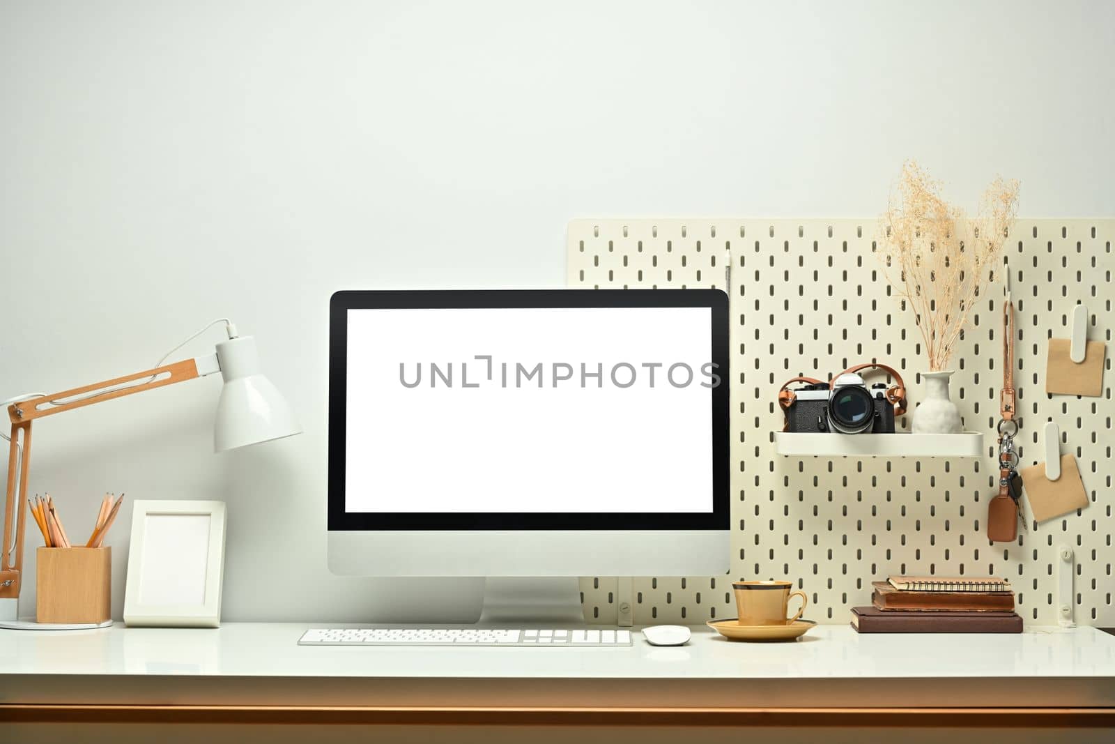 White blank screen computer monitor, picture frame, camera and books on working table. Modern workplace by prathanchorruangsak