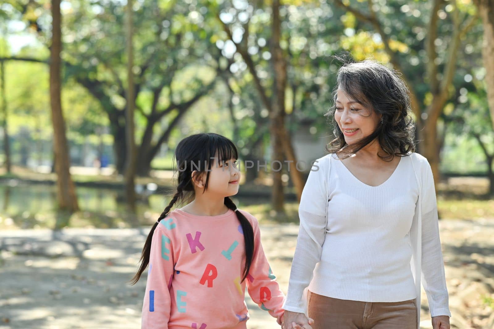 Adorable little child and elderly grandmother walking in the park, spending time outdoor together. Family and love concept.