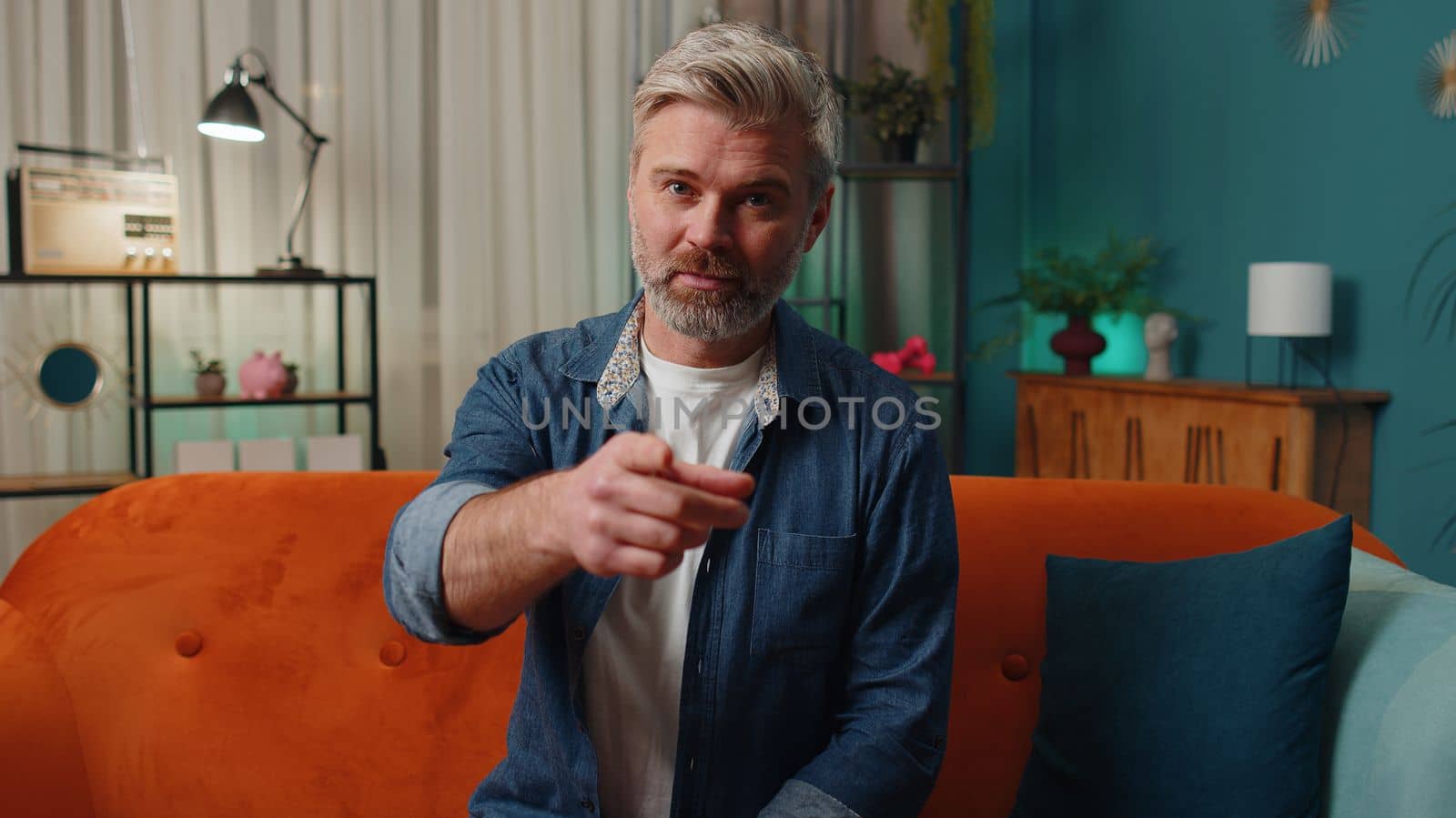 Hey you. Middle-aged old man smiling excitedly and pointing to camera, choosing lucky winner, indicating to awesome you, inviting, approve. Mature senior gray-haired guy at home night room apartment