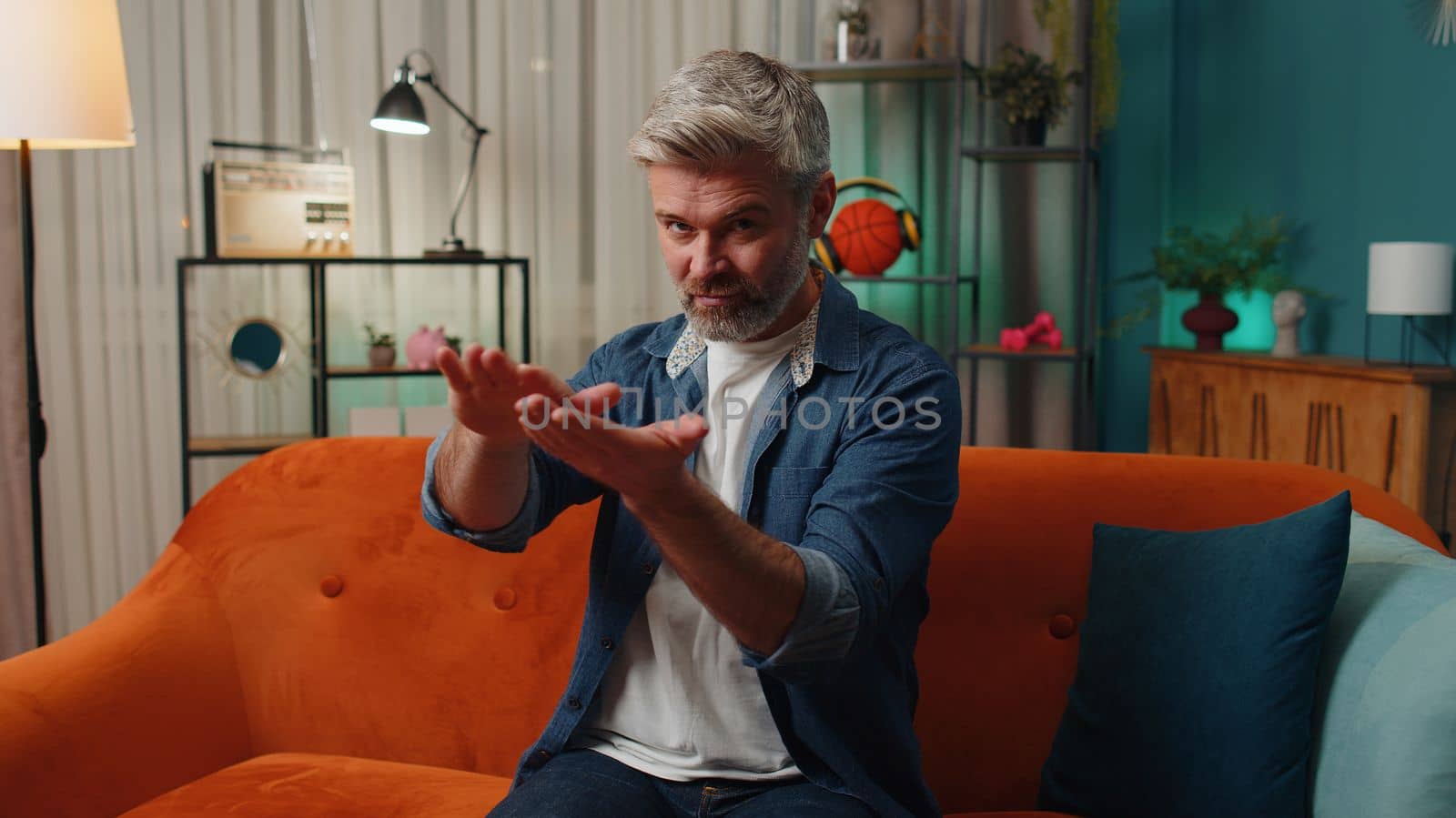 Bearded cheerful rich senior mature man showing wasting, throwing money around hand gesture, more tips earnings, big profit, win lottery, body language, share. Middle-aged guy at home in evening room